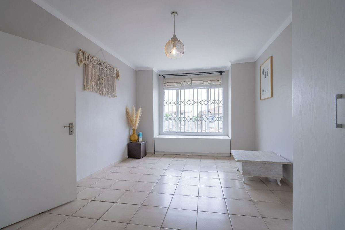 A bright and neutral bedroom featuring tiled flooring, a built-in window seat, and a security gate over the window.