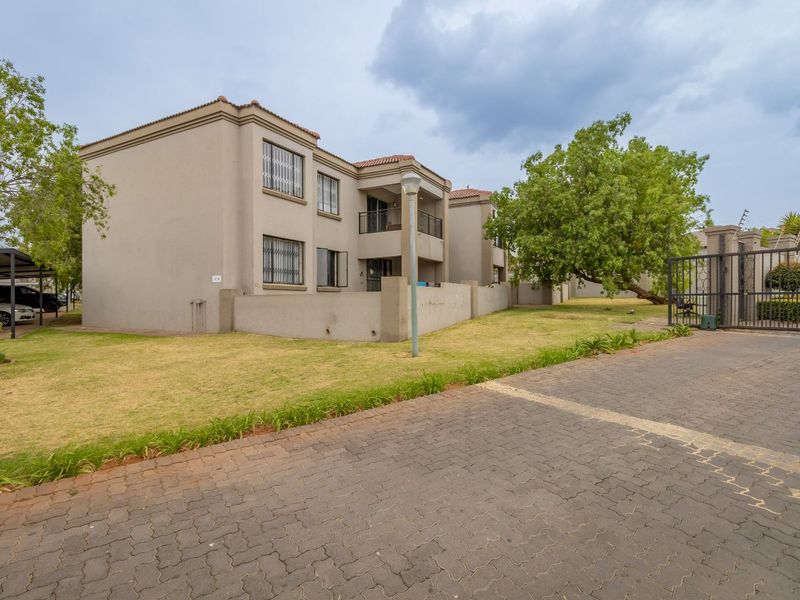 Exterior view of a multi-story apartment complex featuring paved driveway access, security gates, and private balconies with security bars.