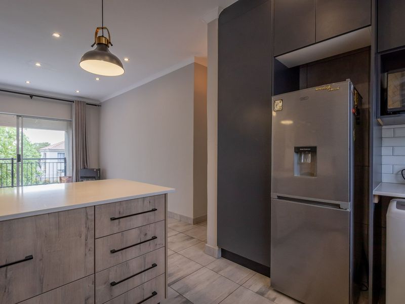 Modern open-plan kitchen featuring a central island, sleek dark cabinetry, subway tile backsplash, and tiled flooring, flowing into a bright living area with balcony access.