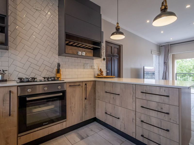 Modern kitchen featuring light wood cabinetry, quartz countertops, a herringbone tile backsplash, and integrated stainless steel oven and gas hob.