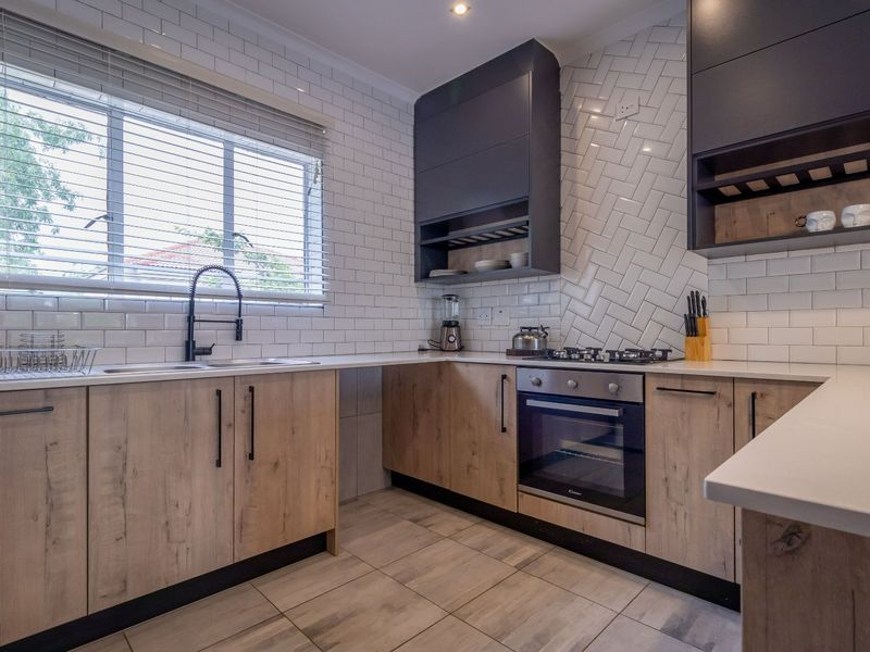 Modern kitchen featuring light wood-finish cabinetry, stone countertops, a stylish herringbone tile backsplash, and integrated stainless steel appliances.