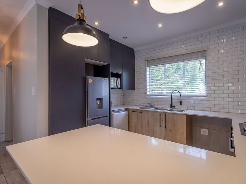 Modern kitchen featuring dark cabinetry, light wood-finish lower cabinets, white subway tile backsplash, quartz countertops, and integrated gas hob.