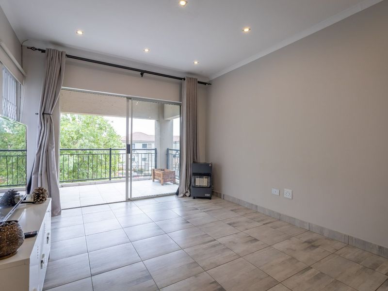 A bright and spacious living area featuring neutral tiled flooring, recessed lighting, and direct access to a private balcony through sliding glass doors.