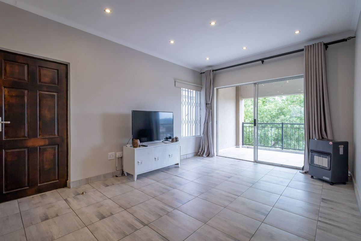 A bright living room featuring neutral tiled flooring, recessed downlighting, and a large sliding glass door providing access to an outdoor balcony area.