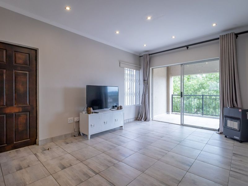 A bright living room featuring neutral tiled flooring, recessed downlighting, and a large sliding glass door providing access to an outdoor balcony area.