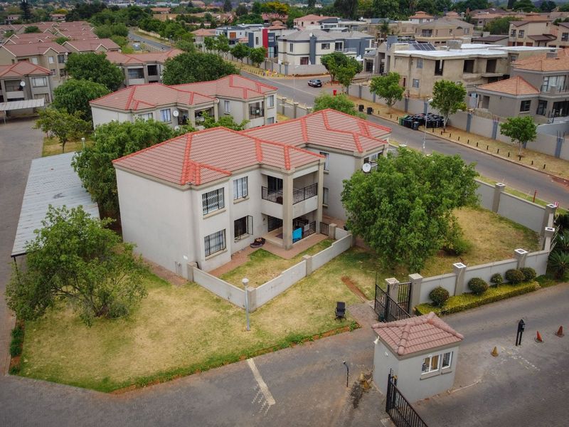 Aerial view of a residential apartment complex featuring tiled roofs, perimeter security walls, a gated entrance with a guard house, and paved driveways.