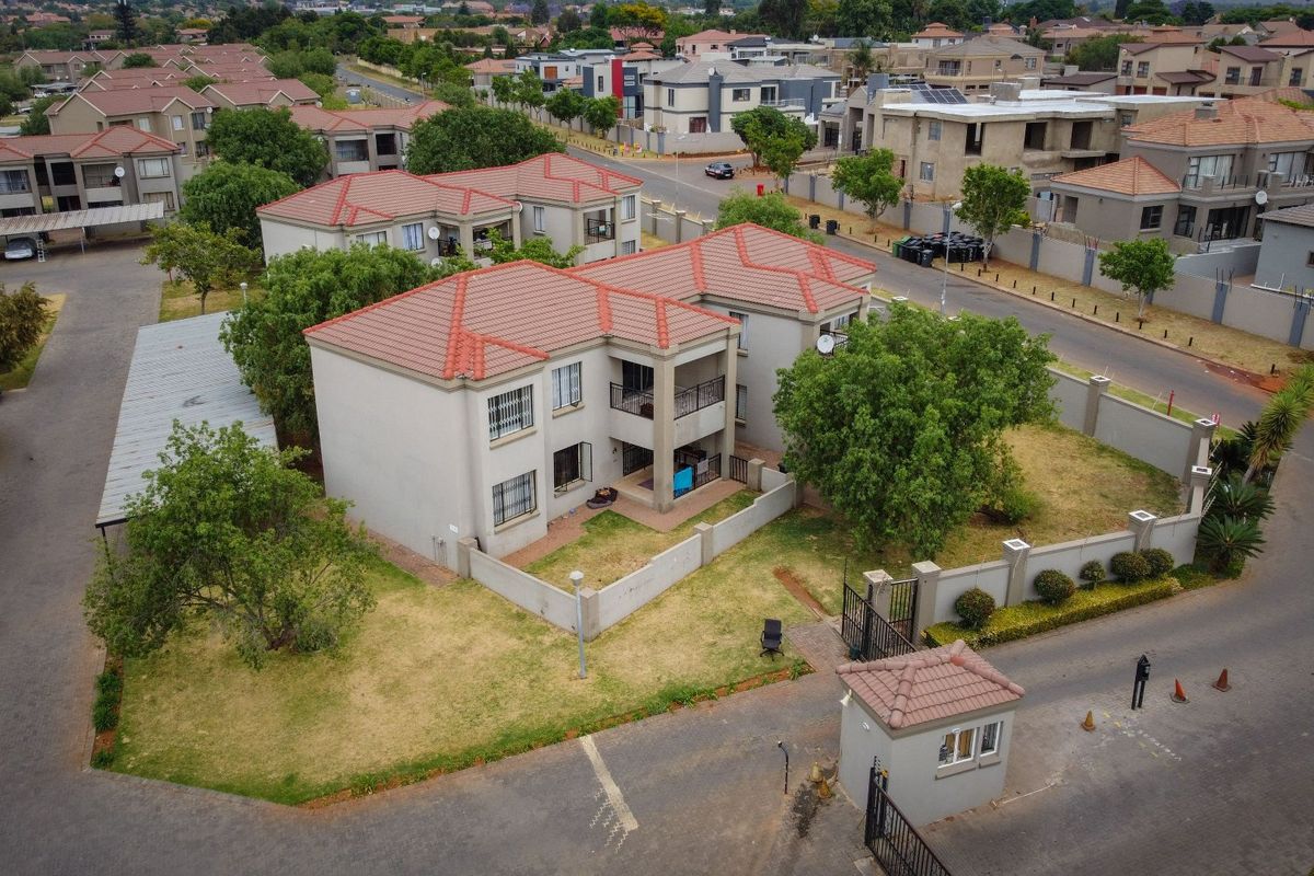 Aerial view of a residential apartment complex featuring tiled roofs, perimeter security walls, a gated entrance with a guard house, and paved driveways.