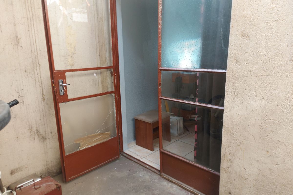 Rear exterior access area featuring metal-framed glass doors with visible damage to the glass and surrounding wall surfaces.