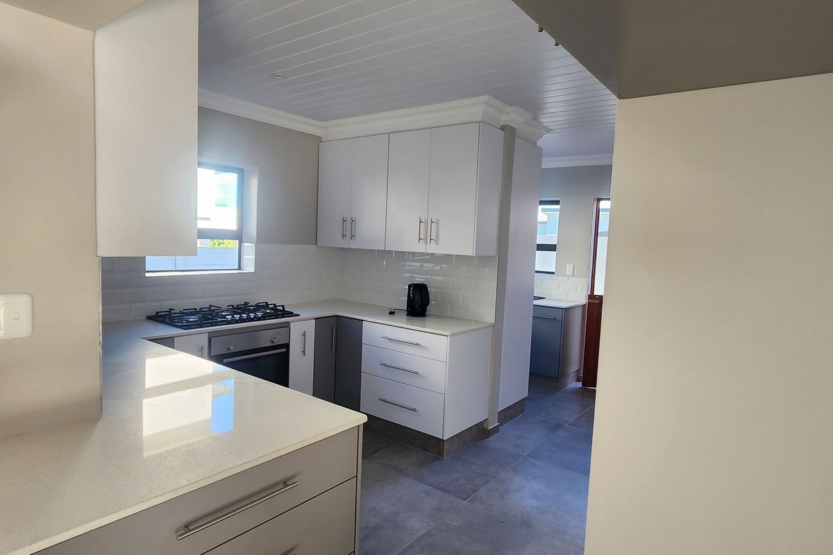 Modern kitchen featuring white cabinetry, stone countertops, a built-in gas hob, and an integrated oven, with a seamless transition to a scullery area.