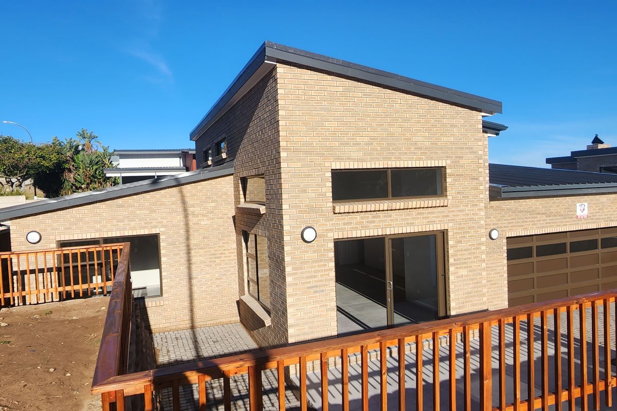 Modern duet property featuring a brick facade, integrated garage, and a wooden deck overlooking an unfinished garden area.