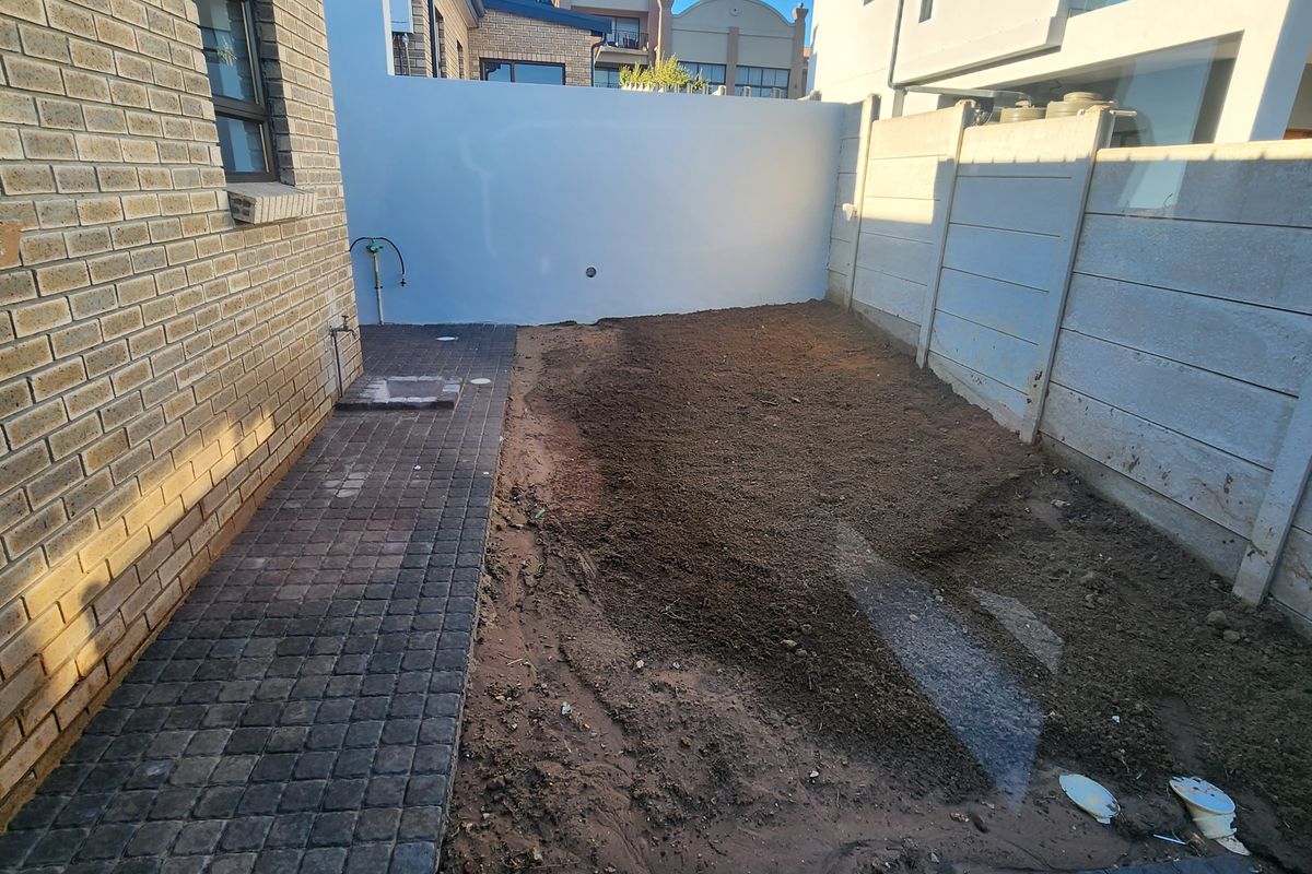 A rear exterior view of a duet property featuring a paved walkway and an unfinished garden area enclosed by boundary walls.
