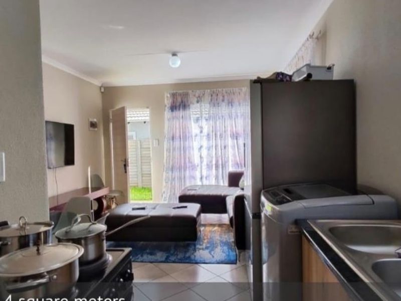 Open plan living area featuring a compact kitchen with double sink and tiled flooring, leading directly to an outdoor patio space.