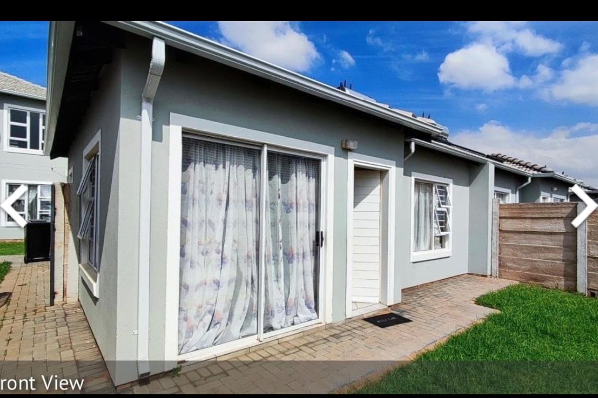 Rear exterior view of the apartment featuring a paved patio area, sliding glass door access, and a private garden space.