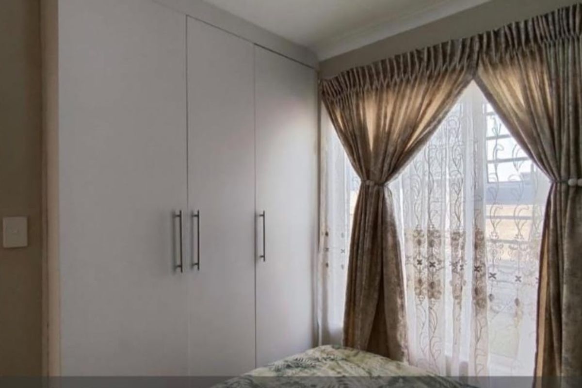 A bedroom featuring built-in cupboards and a window with curtains.