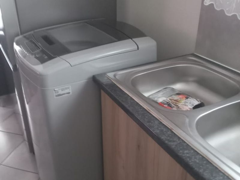 A functional laundry area featuring a stainless steel sink, laminate cabinetry, and tiled flooring, providing essential utility space for the apartment.