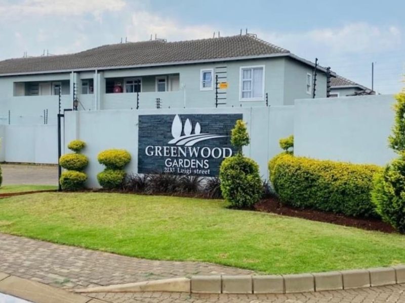 Front entrance view of Greenwood Gardens apartment complex featuring a perimeter wall, electric fencing, and well-maintained landscaped garden.