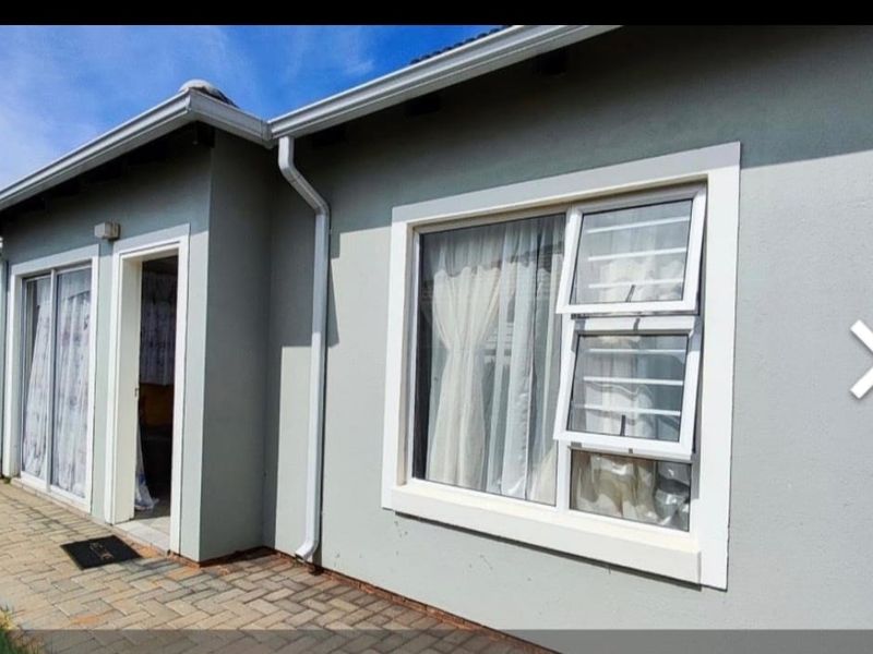 Rear exterior view of the apartment featuring a paved patio area, grey painted walls, and aluminium window frames with security bars.