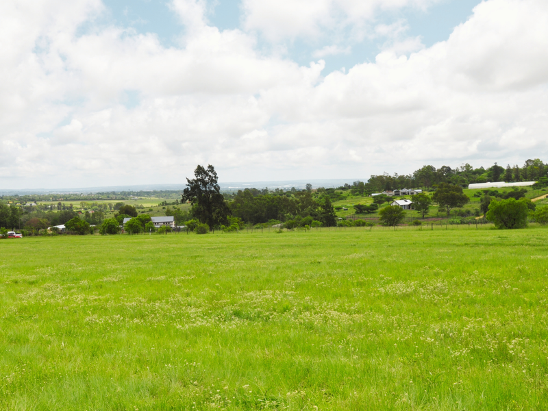 A wide-angle view of a large, open residential vacant land plot featuring expansive green pasture and distant rural landscape.