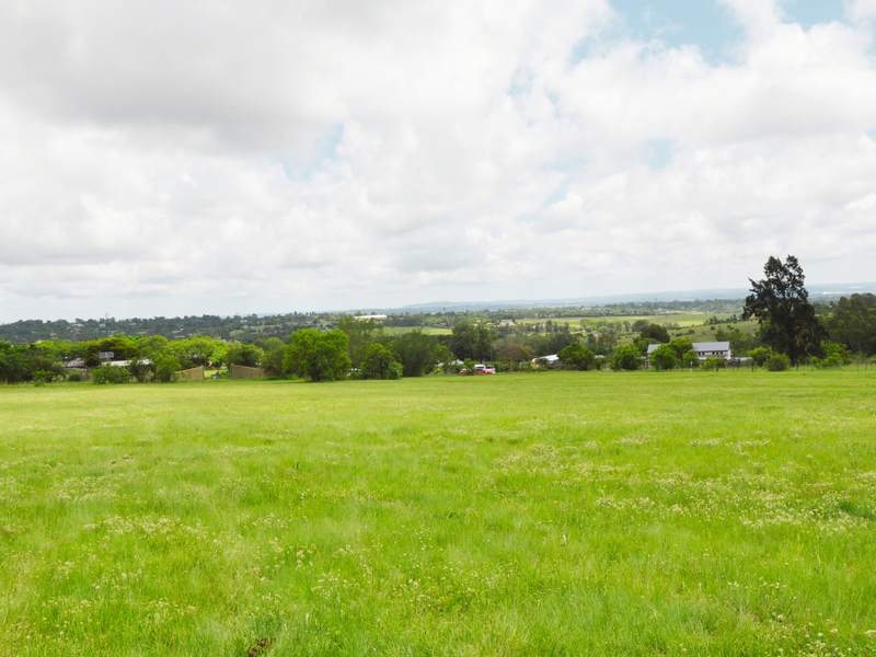 A wide-angle view of a vacant residential plot featuring expansive green grassland and distant landscape views.