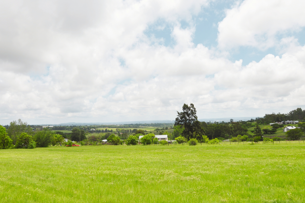 A wide-angle view of the expansive vacant residential land featuring lush green grass, mature trees, and distant rural landscape views.