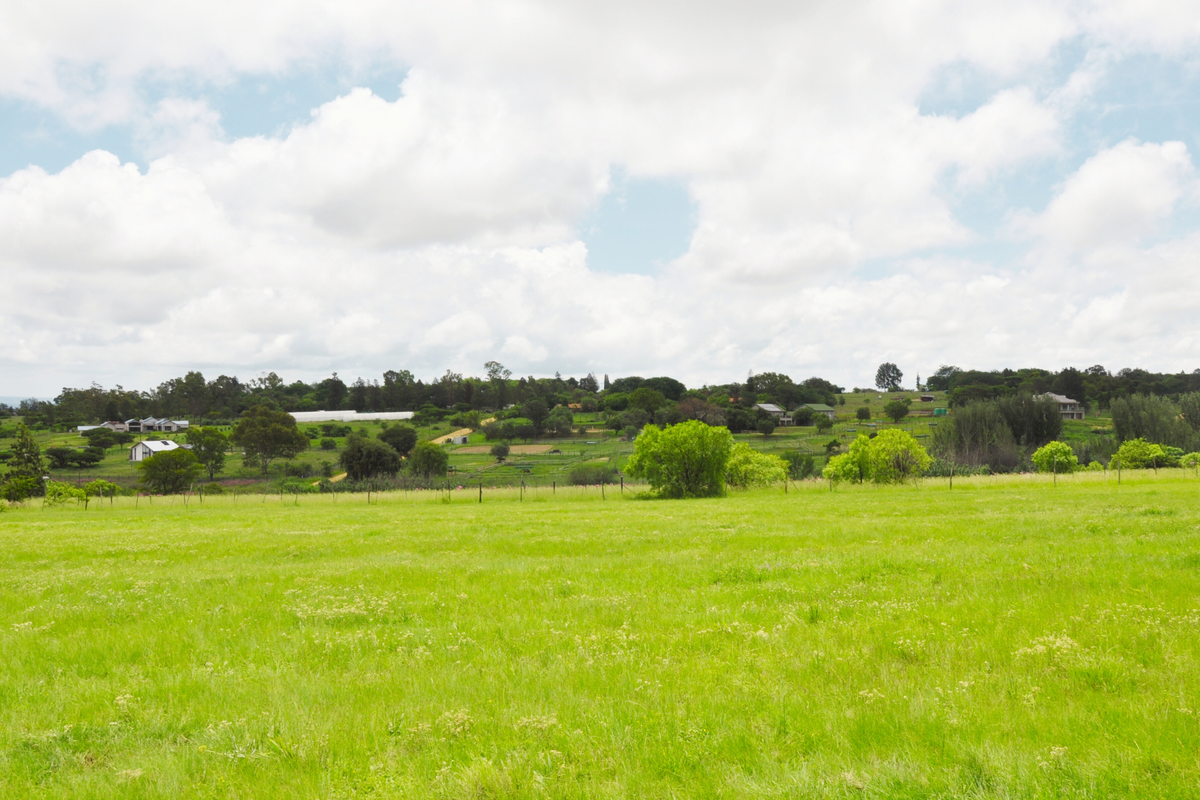 A wide-angle view of a vacant residential plot featuring expansive green grass and surrounding landscape.
