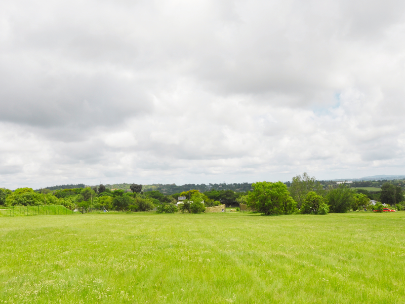 A wide, open expanse of vacant residential land featuring established grass and surrounding greenery, offering a blank canvas for future development.