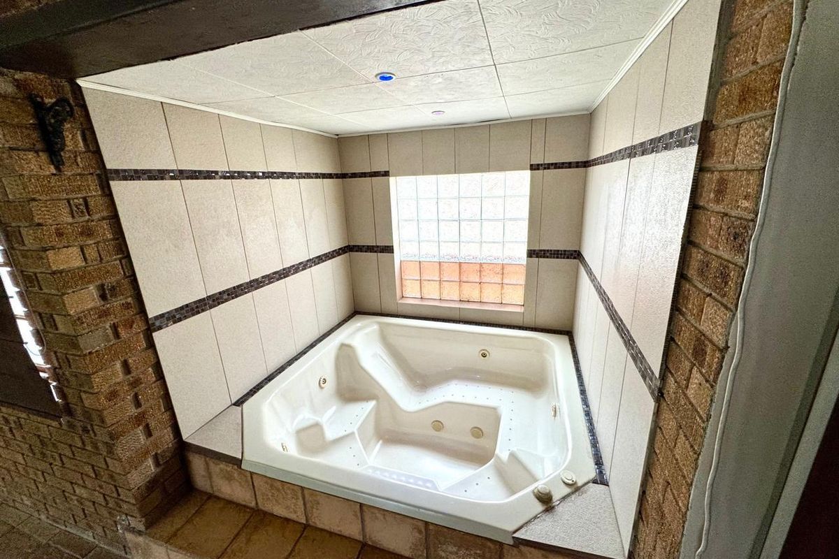 A built-in spa bath set within a tiled alcove featuring a glass block window and exposed brick wall accents.