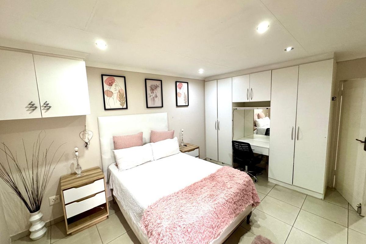 A well-maintained bedroom featuring neutral tiled flooring, extensive built-in cabinetry with an integrated vanity, and recessed ceiling lighting.