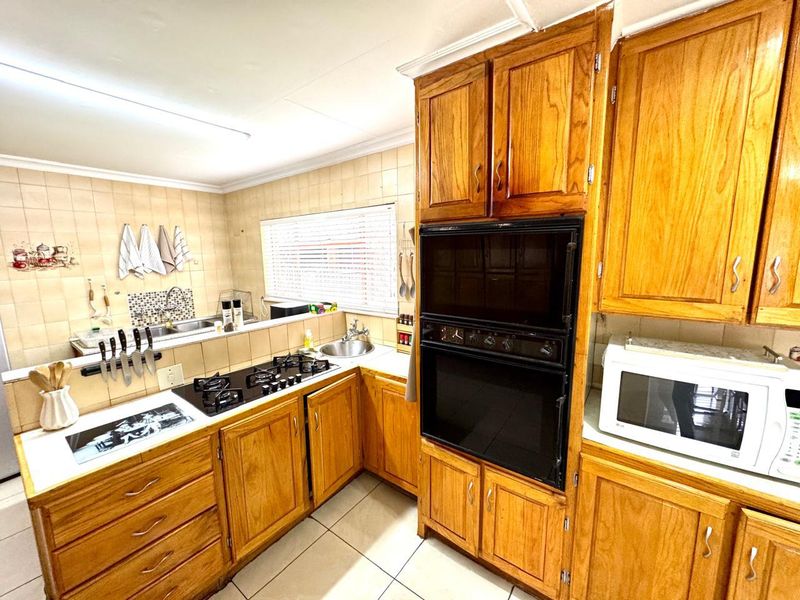 A functional kitchen featuring traditional wooden cabinetry, a built-in oven, gas hob, and tiled finishes, offering a classic layout with ample storage space.