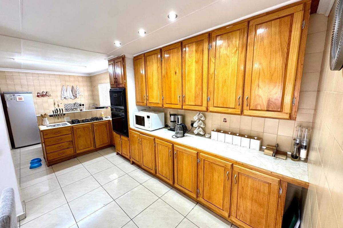 A functional kitchen featuring extensive wooden cabinetry, tiled flooring, a built-in oven, and a gas hob with a tiled backsplash.