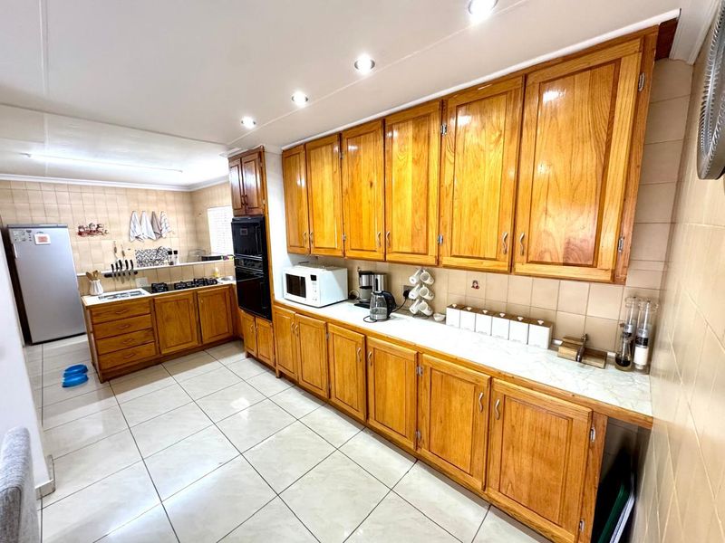 A functional kitchen featuring extensive wooden cabinetry, tiled flooring, a built-in oven, and a gas hob with a tiled backsplash.