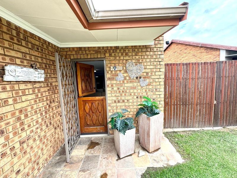 A rear exterior view featuring a brick facade, a timber stable-style door with a security gate, and a stone-paved patio area.