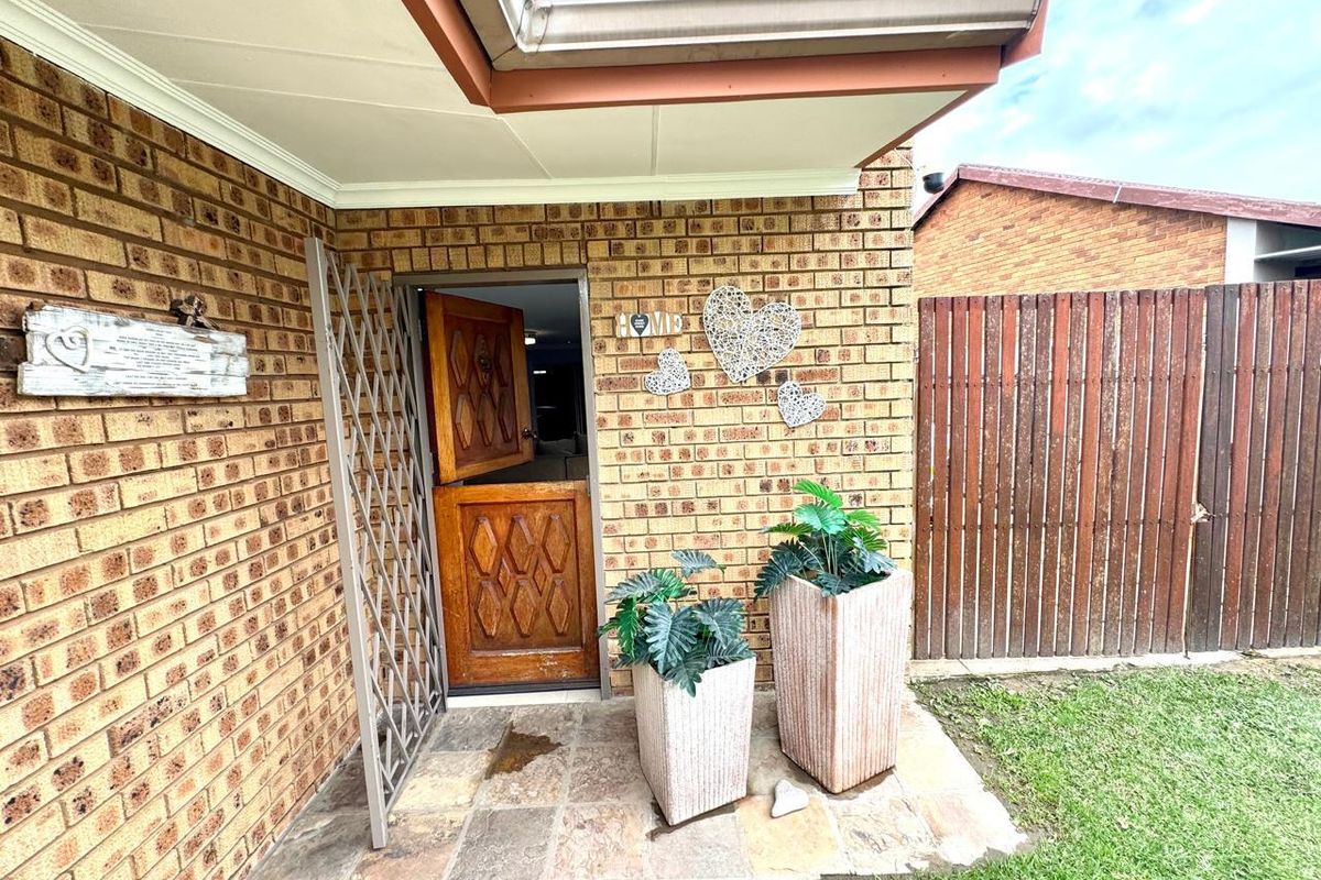 A rear exterior view featuring a brick facade, a timber stable-style door with a security gate, and a stone-paved patio area.