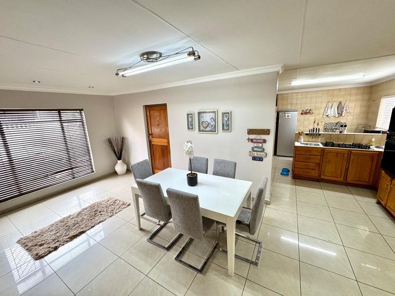 Open-plan dining area flowing into a functional kitchen with wooden cabinetry, tiled floors, and modern lighting fixtures.
