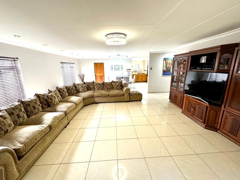 Spacious open-plan living area featuring large format floor tiles, recessed lighting, and neutral walls, with a view through to the kitchen area.
