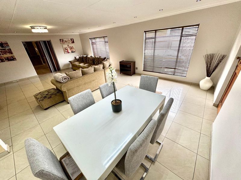 Spacious open-plan living and dining area featuring neutral tiled flooring, recessed downlighting, and large windows with fitted venetian blinds.
