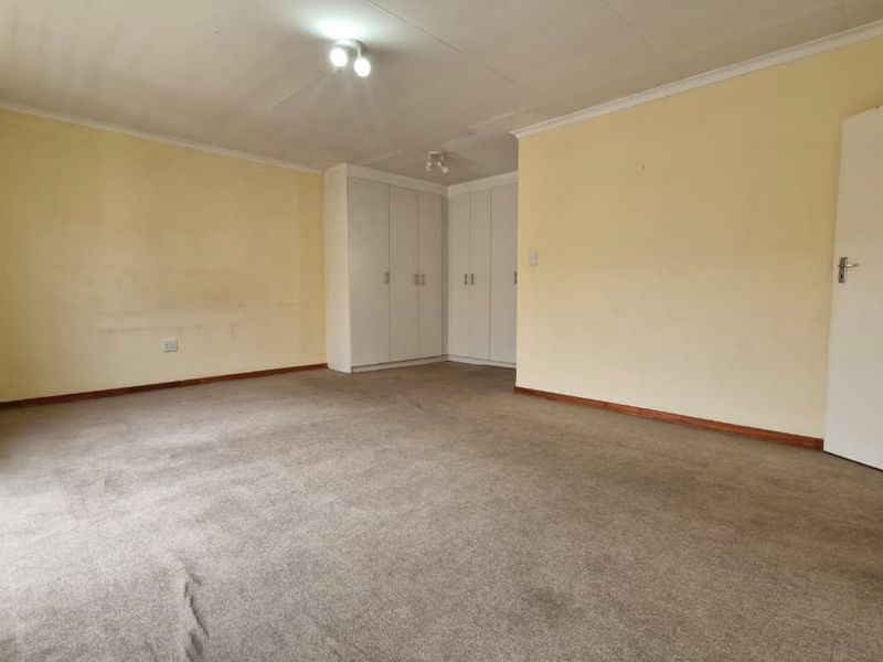 Spacious bedroom featuring built-in cupboards, carpeted flooring, and a security gate, offering a blank canvas for renovation.