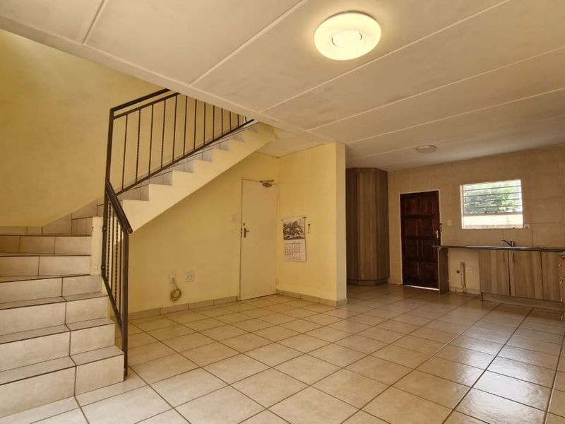 Open plan living area featuring a tiled staircase with metal railing and a functional kitchen with built-in cabinetry and tiled flooring throughout.