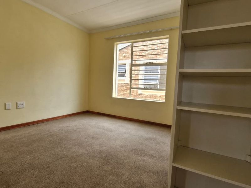 A vacant bedroom featuring neutral walls, carpeted flooring, and built-in shelving, offering a blank canvas for personalization.