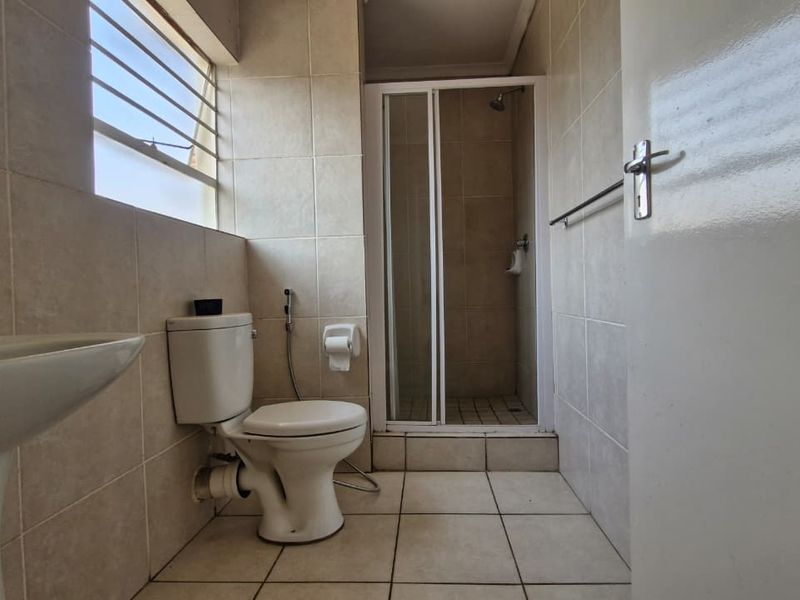 A functional bathroom featuring a pedestal basin, toilet, and a separate shower enclosure with neutral wall and floor tiling.