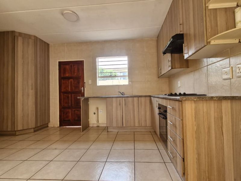 A functional kitchen featuring wood-look cabinetry, built-in oven and hob, tiled surfaces, and direct access to an exterior door.