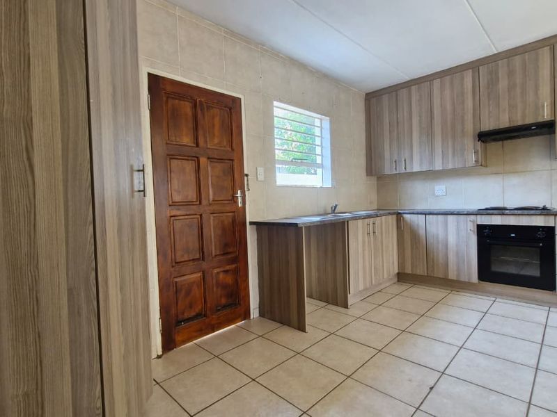 A functional kitchen featuring wood-look cabinetry, built-in oven and hob, tiled flooring, and a tiled backsplash, offering a clean and practical workspace.