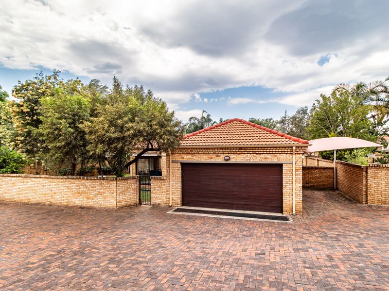 Front exterior view of the townhouse featuring a paved driveway, brick perimeter wall, and a single garage with a tiled roof.