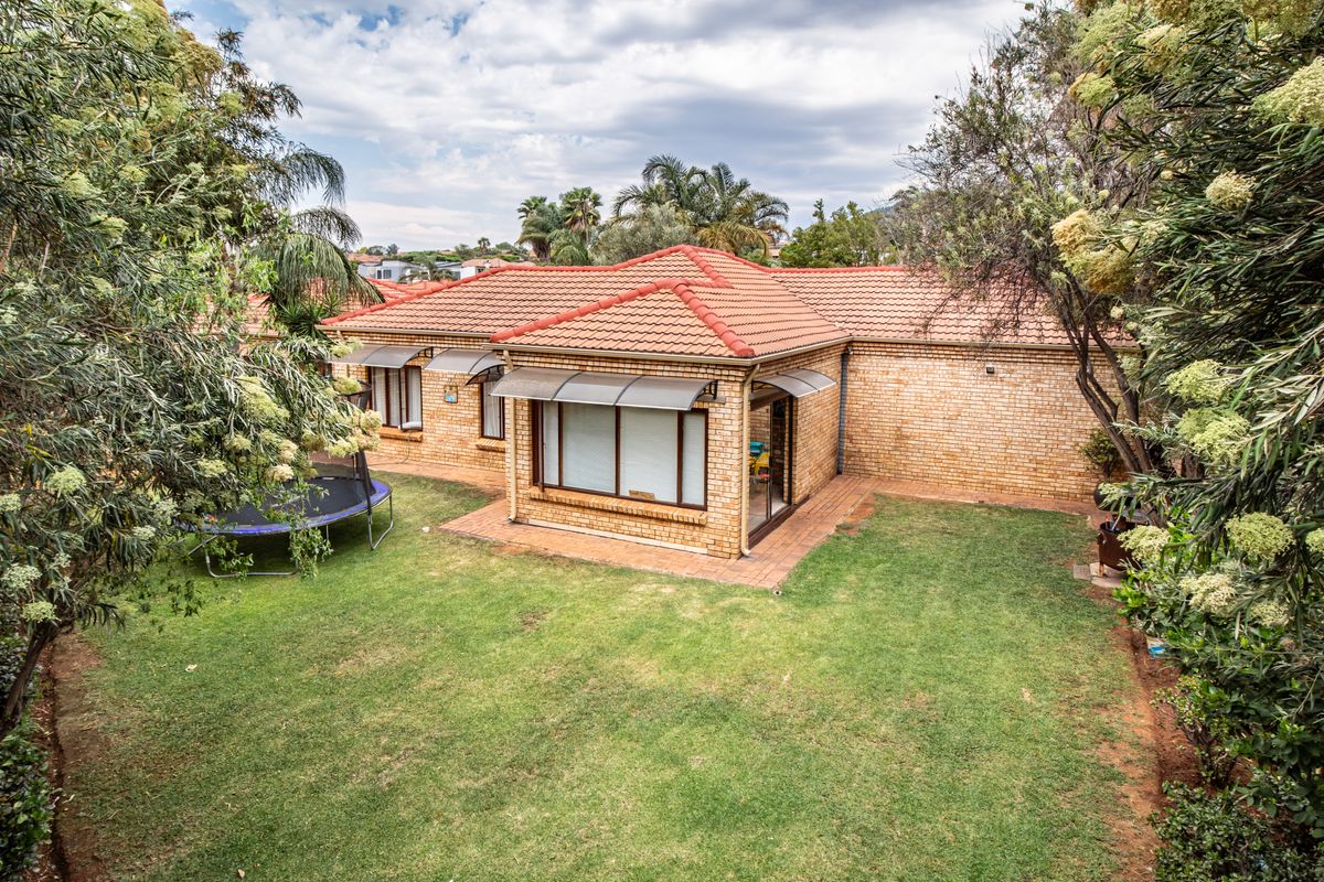 Rear view of a face brick townhouse featuring a tiled roof, paved patio area, and established garden surroundings.