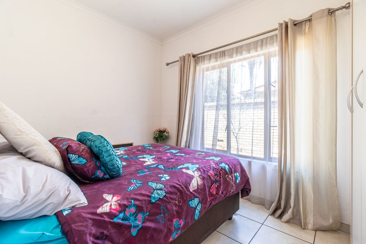 A bedroom featuring tiled flooring and a built-in wardrobe, with natural light entering through a window fitted with a curtain rod.