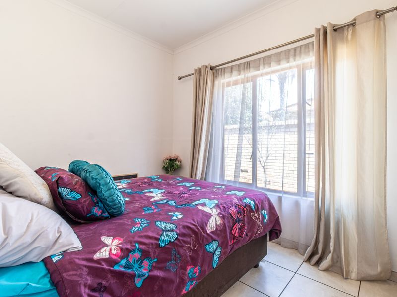 A bedroom featuring tiled flooring and a built-in wardrobe, with natural light entering through a window fitted with a curtain rod.