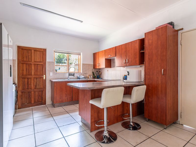 Functional kitchen featuring wood-look cabinetry, a breakfast bar, tiled flooring, and a tiled backsplash with direct access to an exterior door.