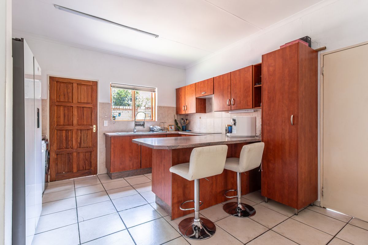 Functional kitchen featuring wood-look cabinetry, a breakfast bar, tiled flooring, and a tiled backsplash with direct access to an exterior door.