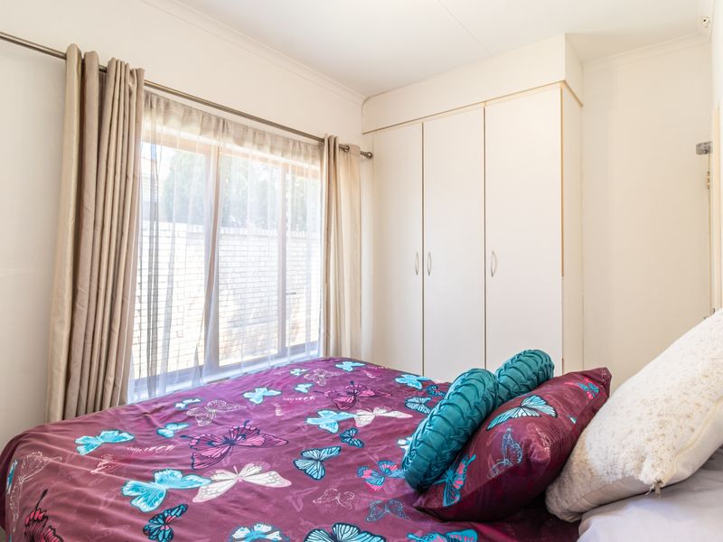 A functional bedroom featuring a built-in wardrobe and large window with curtain rod, providing natural light and storage space.