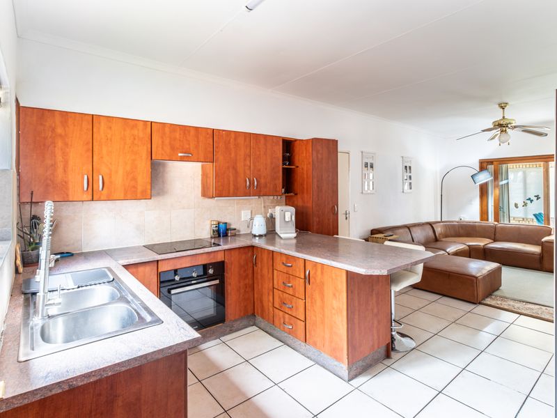 Open-plan kitchen and living area featuring wooden cabinetry, laminate countertops, built-in oven, electric hob, and tiled flooring throughout.